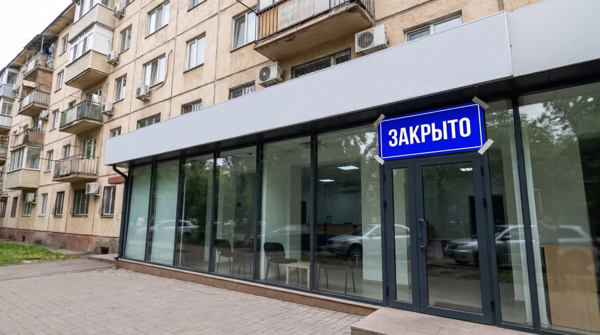 Закрытый филиал микрофинансовой организации в Алматы: советская пятиэтажка, пустая стеклянная витрина без брендинга, на двери большая ярко-синяя табличка ЗАКРЫТО